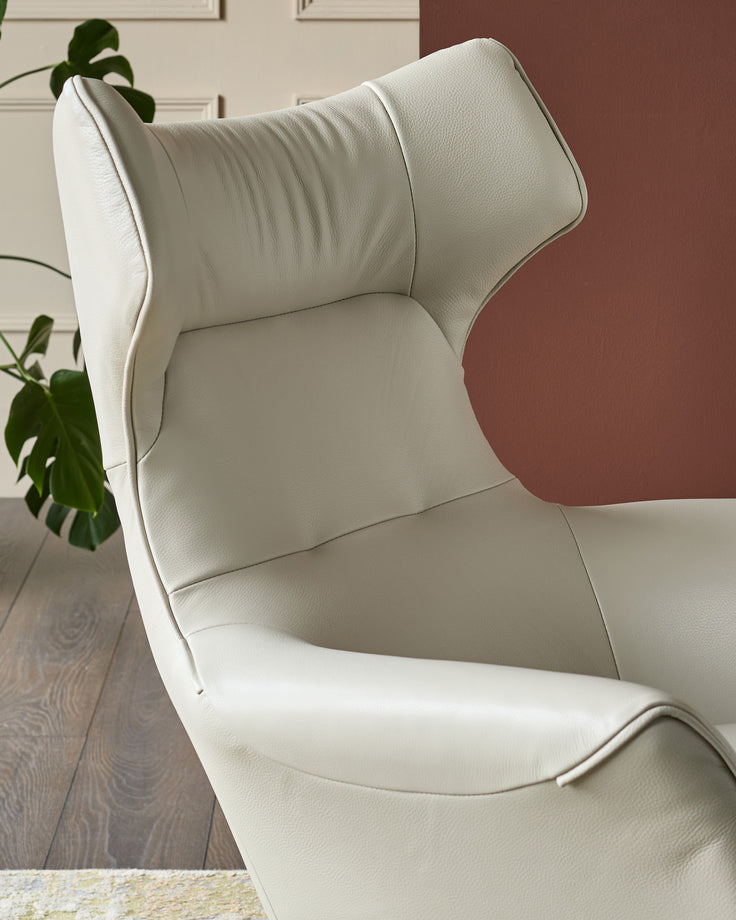 Reign Occasional Chair in natural grey leather, shown at a side angle highlighting its curved high back and cushioned seat.