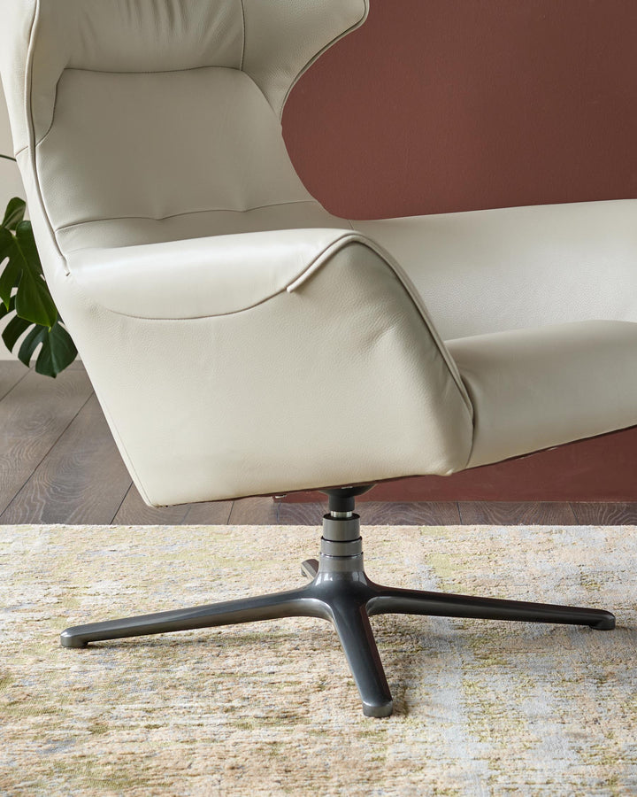 Reign occasional chair in natural grey leather, shown from side angle with black pedestal base and burgundy headrest panel.