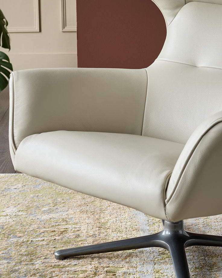Cream leather occasional chair with curved backrest and black pedestal base, shown in room setting.