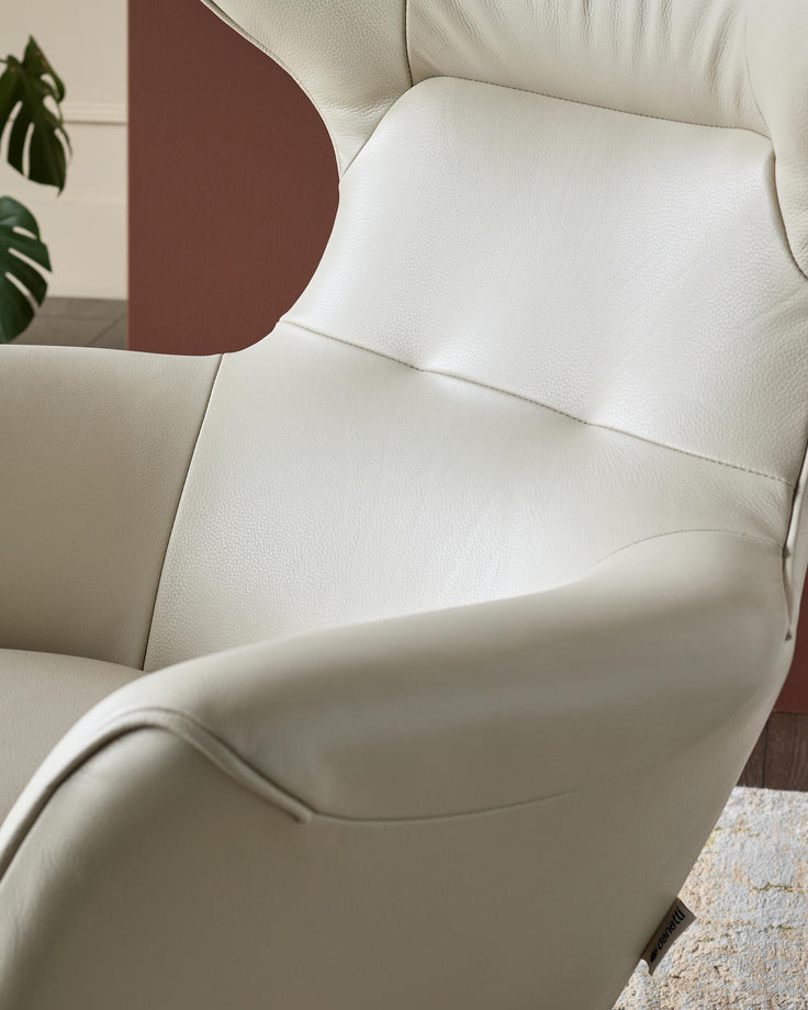 Cream leather occasional chair with curved armrests and padded seat, shown from above at an angle in a styled room setting.