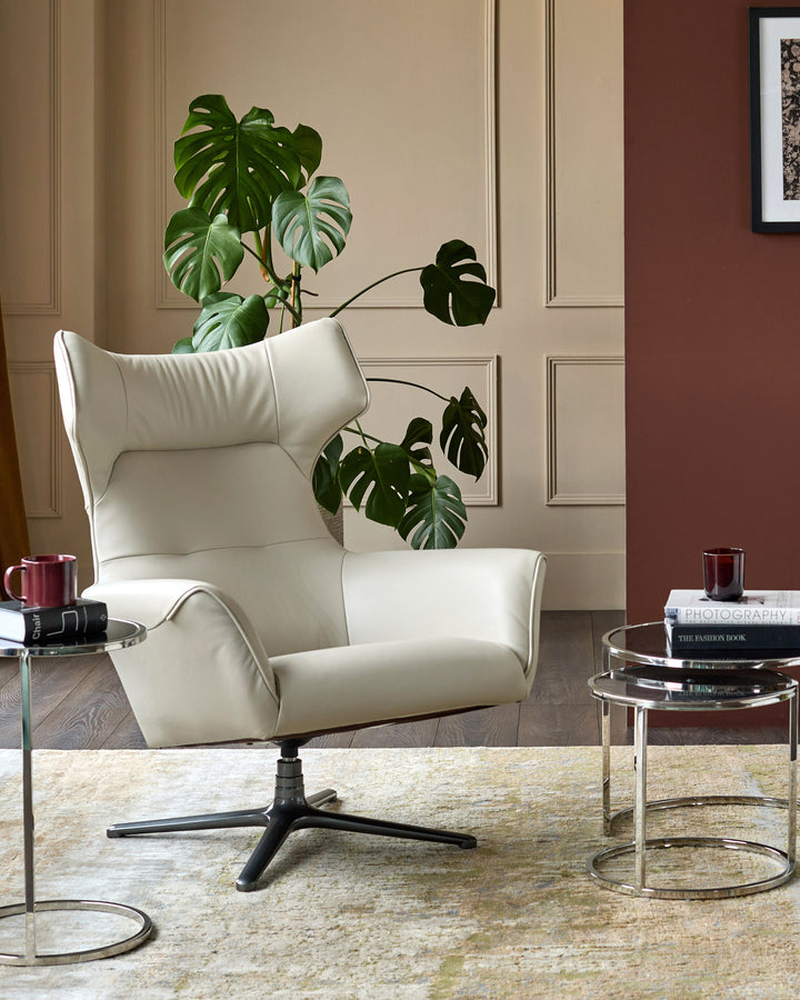 Cream leather lounge chair with high backrest and black swivel base, displayed in a styled living room setting.