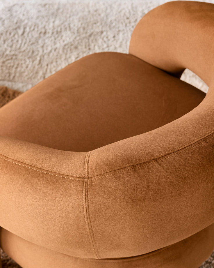 Caramel fabric accent chair shown in close-up detail, highlighting curved armrest and plush upholstery texture.