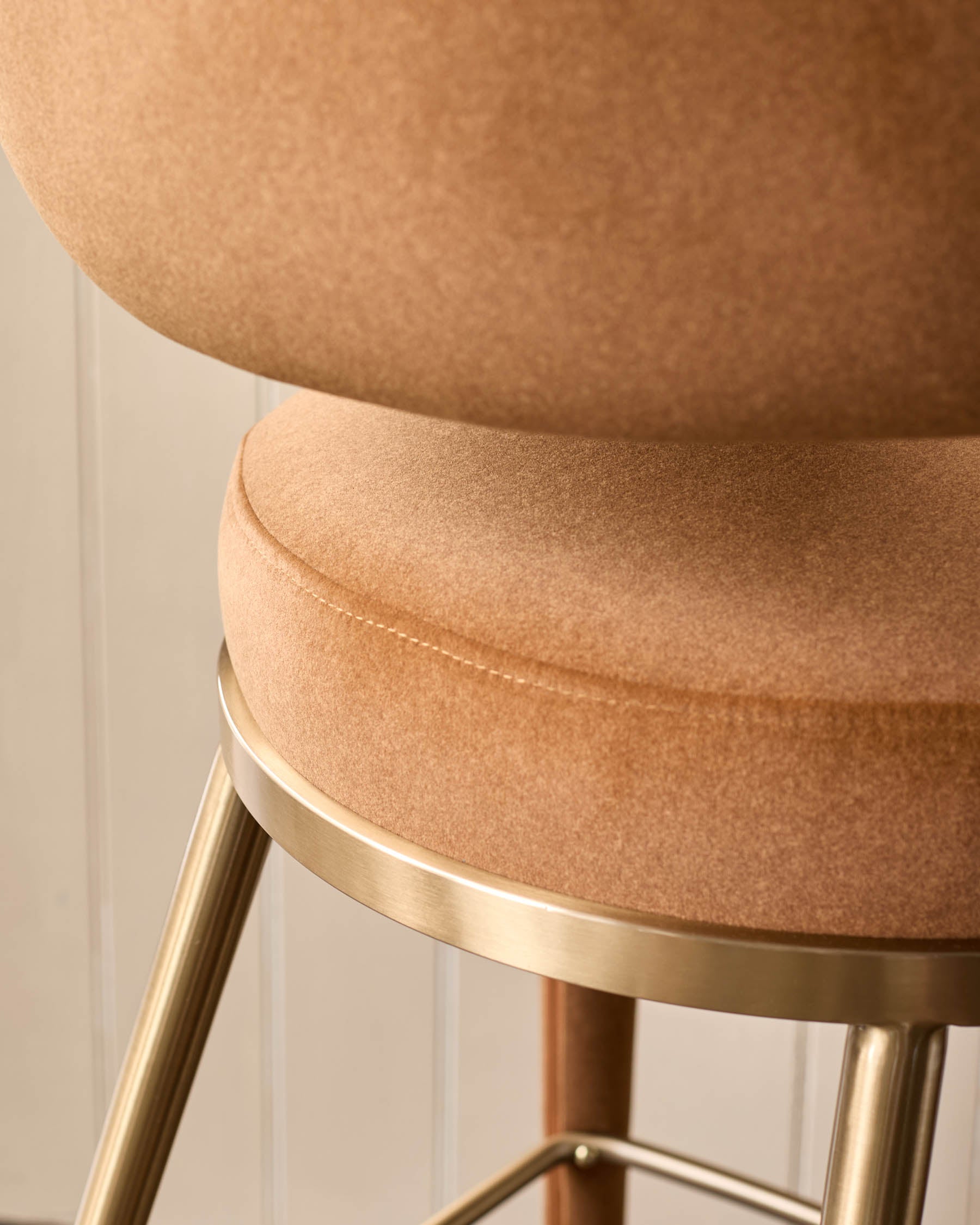 A stylish bar stool featuring a plush, tan seat and sleek gold legs, perfect for adding a touch of modern elegance to any space.