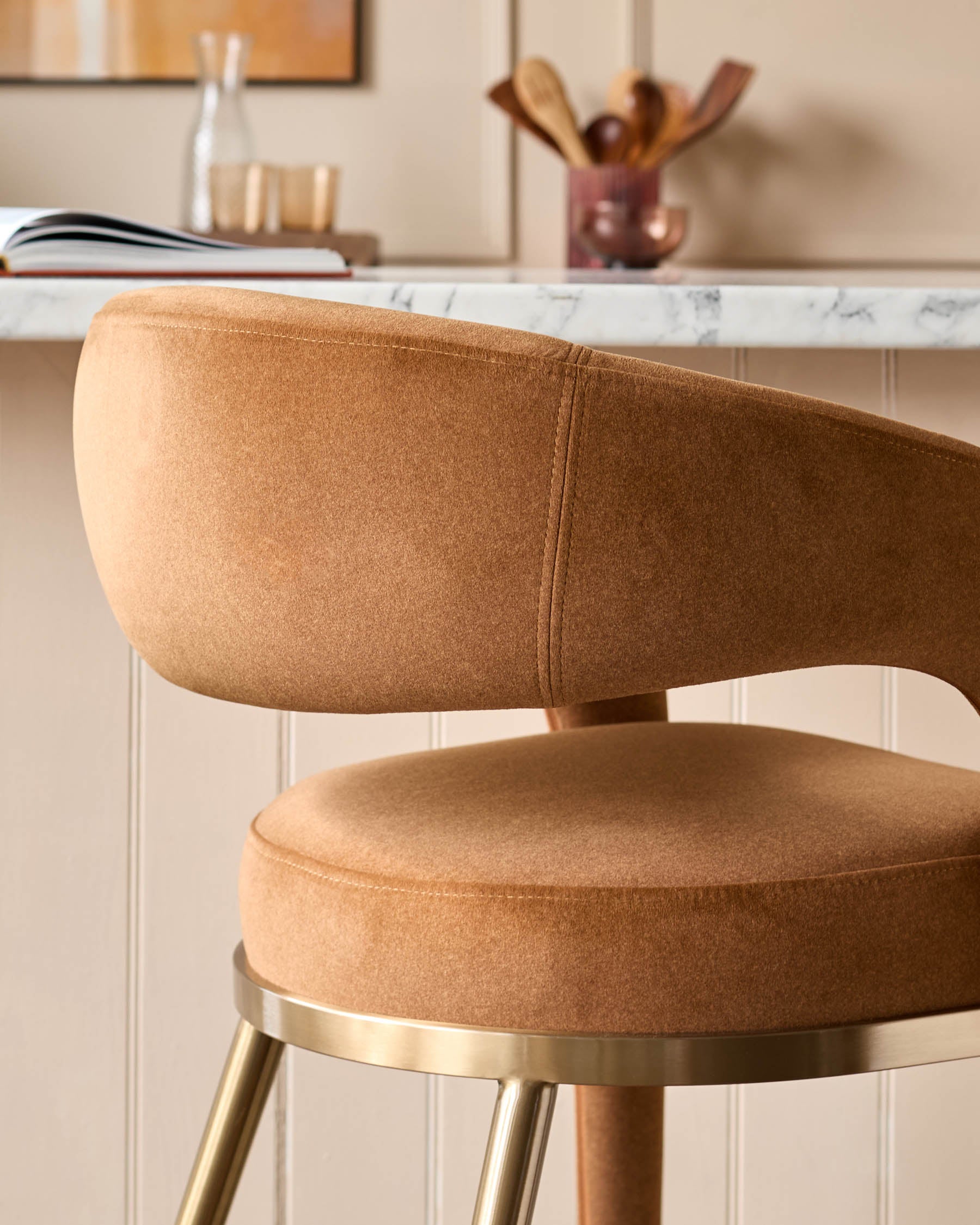 A stylish tan upholstered bar stool with a gold metal base complements the neutral kitchen decor.