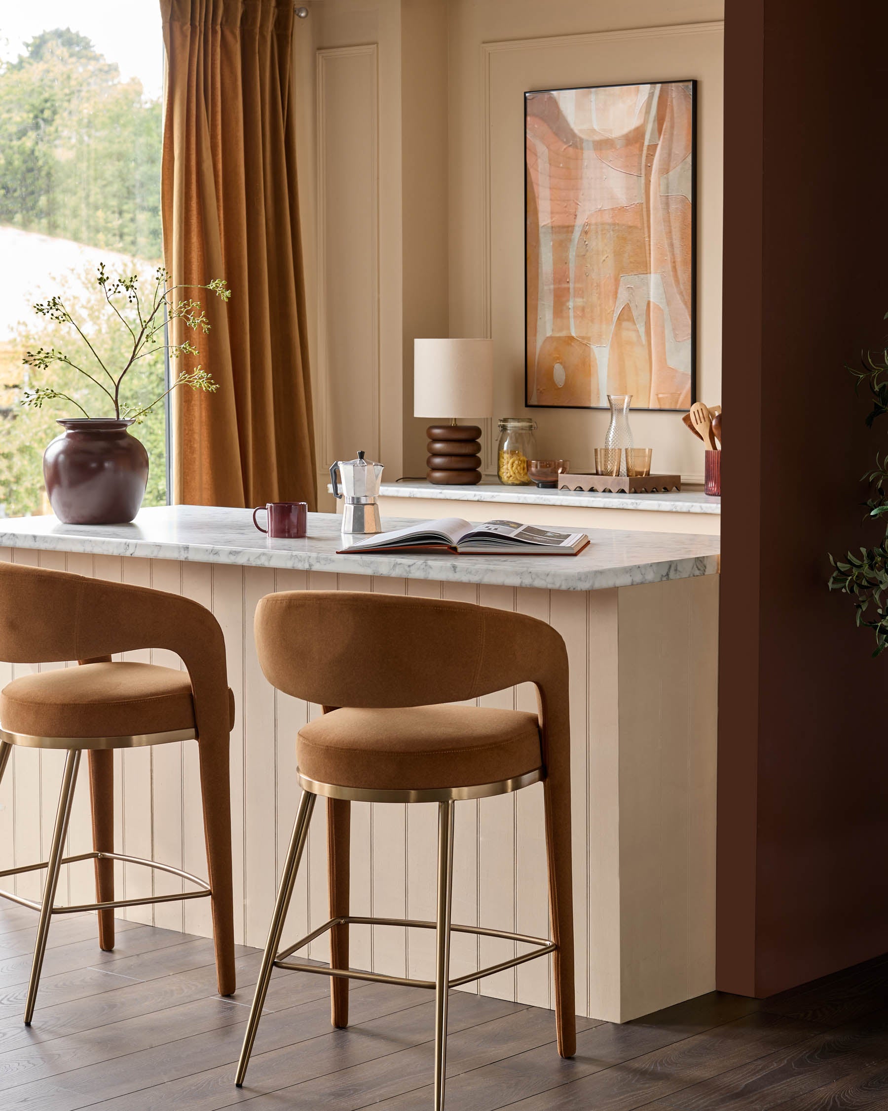 Two stylish brown bar stools with gold legs sit in front of a kitchen island, exuding warmth and sophistication.