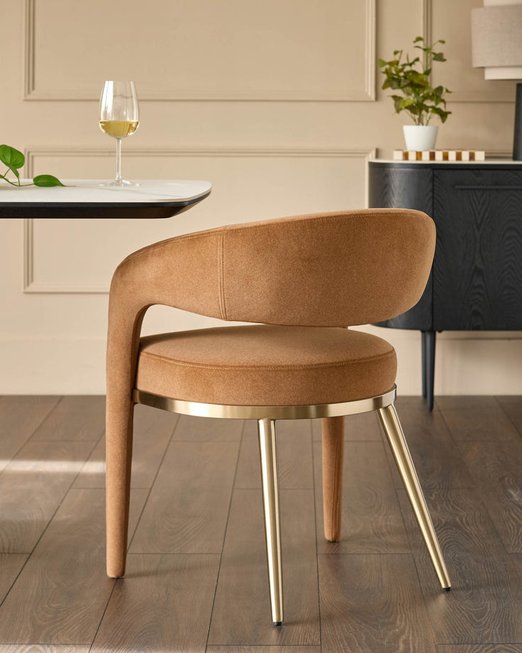 Stylish tan chair with gold legs sits beside a modern table and dark wood sideboard, adding a touch of class to any dining space.