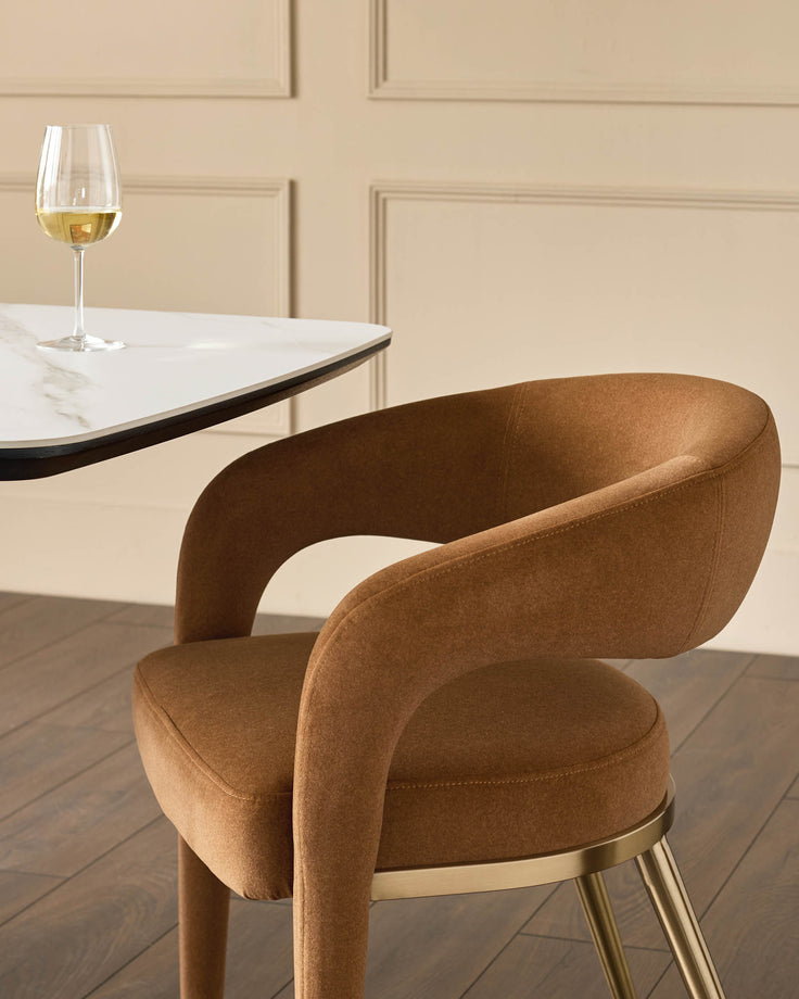 A stylish brown upholstered chair with a curved back, paired with a modern table and a wine glass.