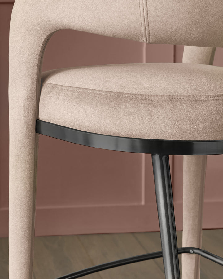 Rhett bar stool in champagne velvet with curved backrest and black metal footrest detail, side view.