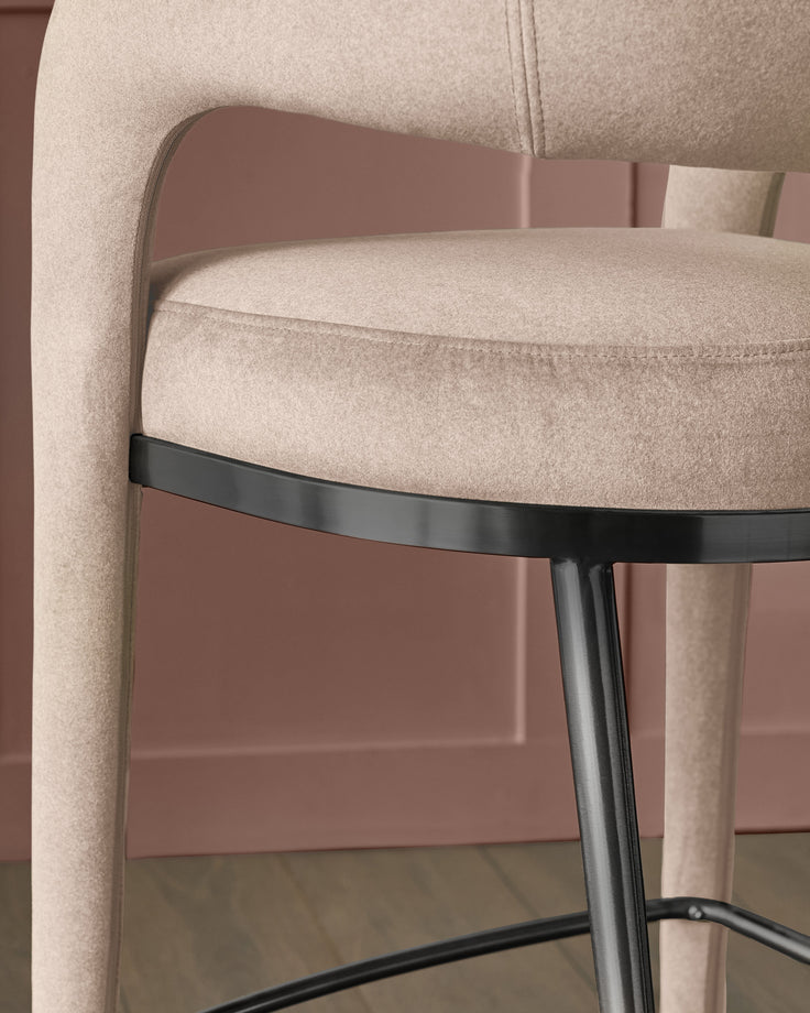 Rhett bar stool in champagne velvet with curved backrest and black metal footrest detail, side view.
