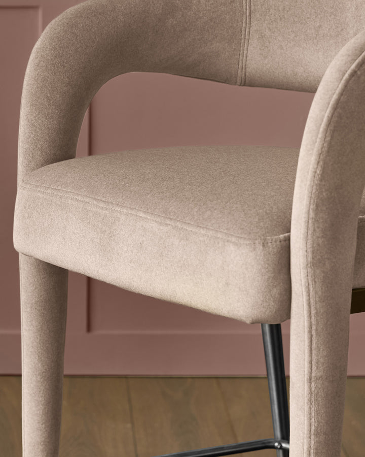 Champagne velvet bar stool with curved arms, cylindrical legs, and black metal base against mauve wall.