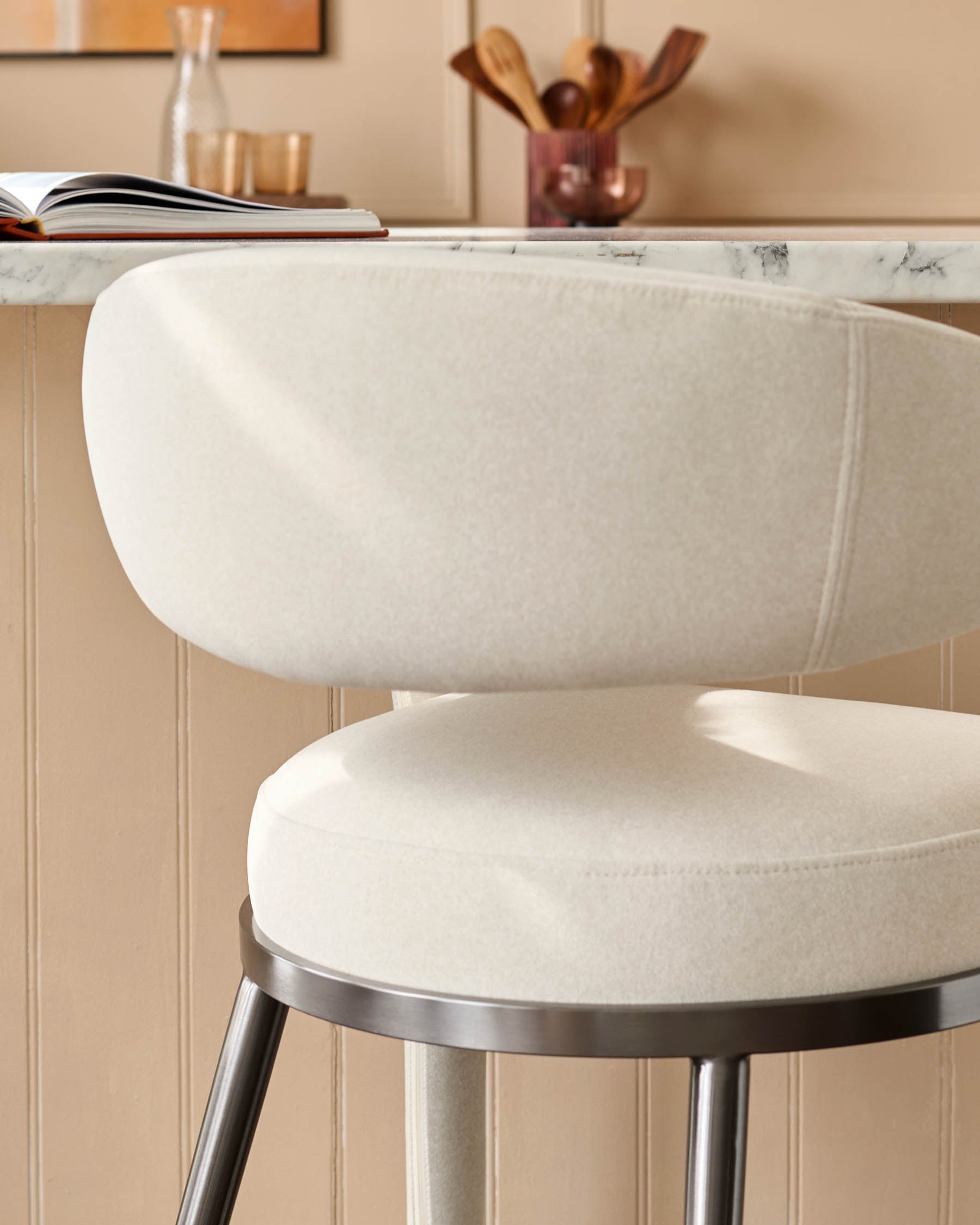 Close-up of a modern bar stool with a curved, cream-coloured seat and back, and a sleek, metallic base.