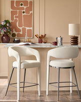 Two stylish bar stools with curved, off-white upholstery and metal legs sit at a kitchen counter.