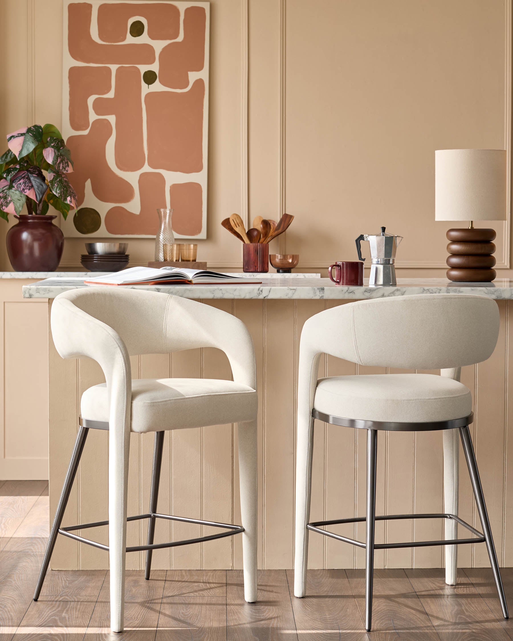 Two stylish bar stools with curved, off-white upholstery and metal legs sit at a kitchen counter.