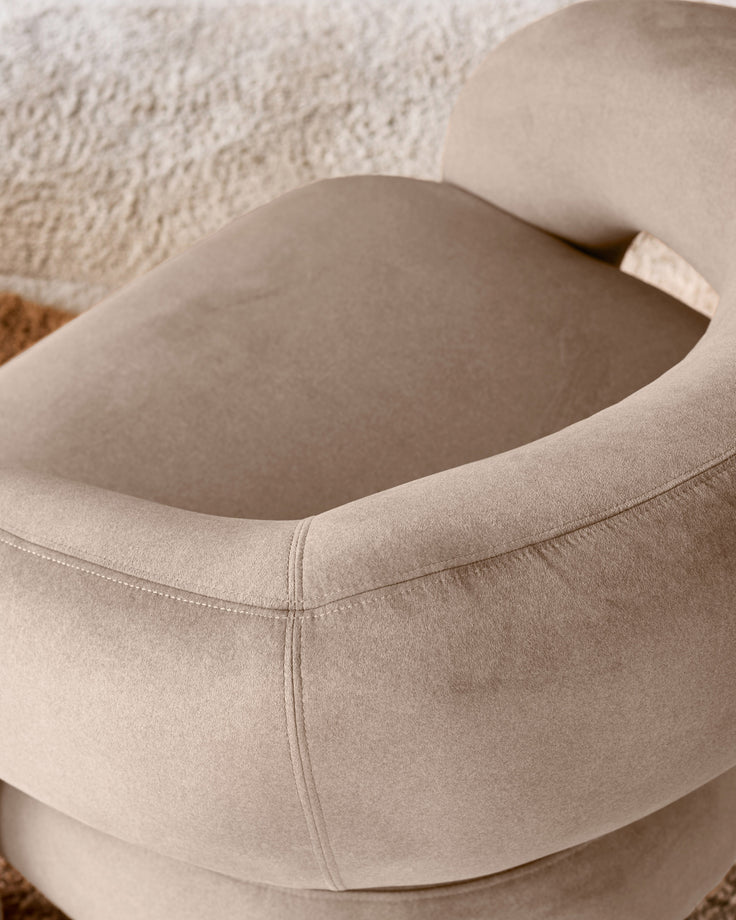 Rhett accent chair in natural fabric, close-up of curved armrest and seat detail against textured wall.