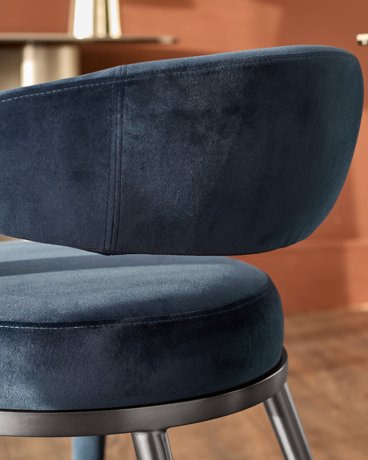Rhett dining chair in dark navy velvet, close-up detail of curved backrest and seat with metal base.