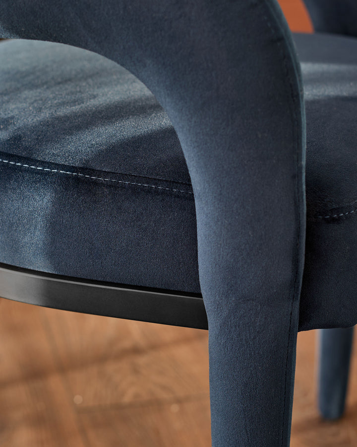 Rhett dining chair in dark navy velvet, close-up of curved backrest and stitched seam detail with wooden leg visible.