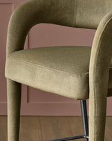 Rhett bar stool in olive green fabric with curved backrest and black metal legs, side angle view.