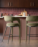Olive green fabric bar stools with curved backrest and black metal legs at kitchen island with burgundy cabinetry.