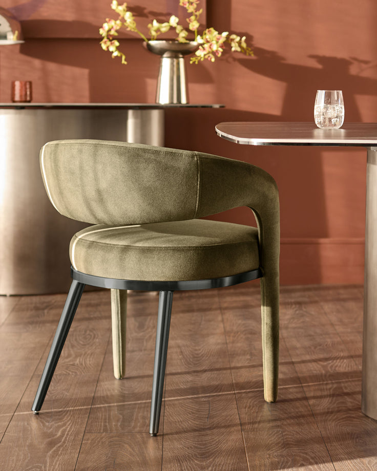 Rhett dining chair in olive green fabric with curved backrest, metal legs, shown in room setting at table.