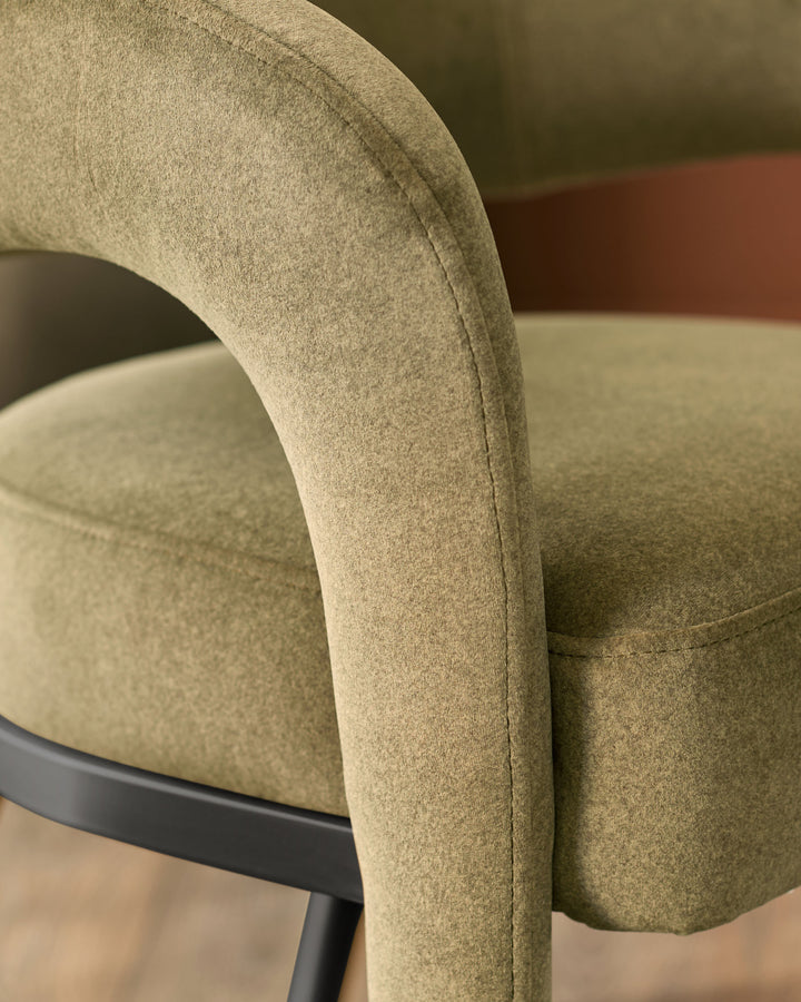 Rhett dining chair in olive green fabric, close-up detail of curved armrest and seat with black metal base.