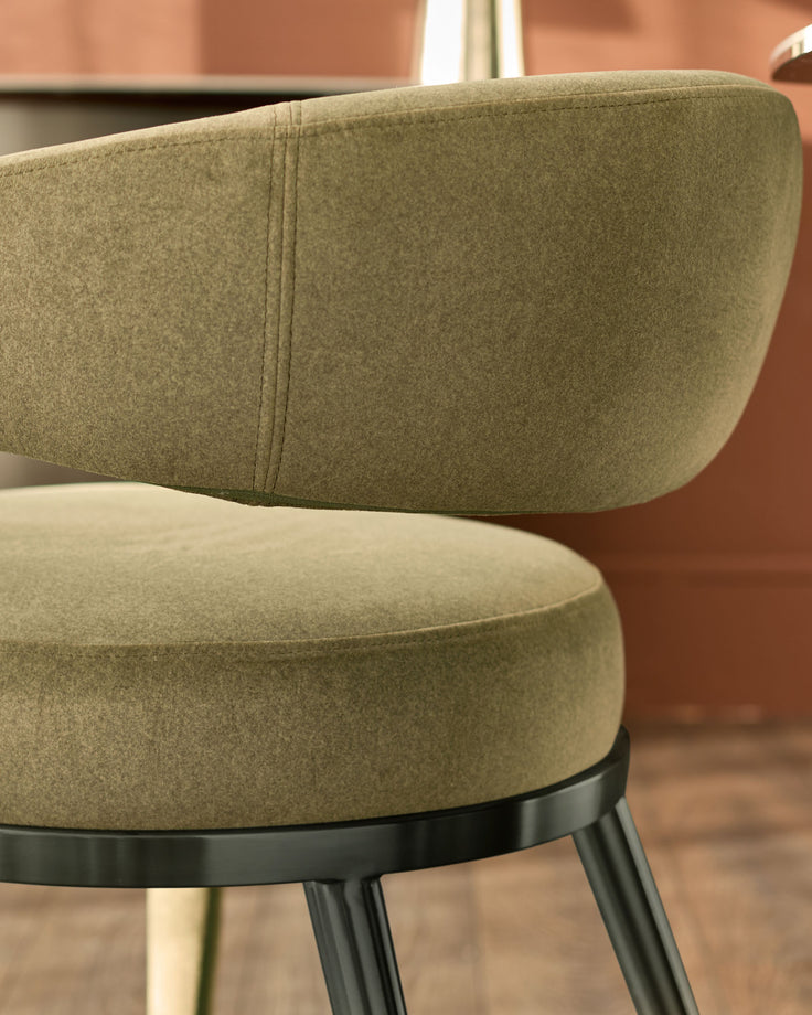 Rhett dining chair in olive green fabric, shown in close-up detail highlighting the curved backrest and black metal legs.
