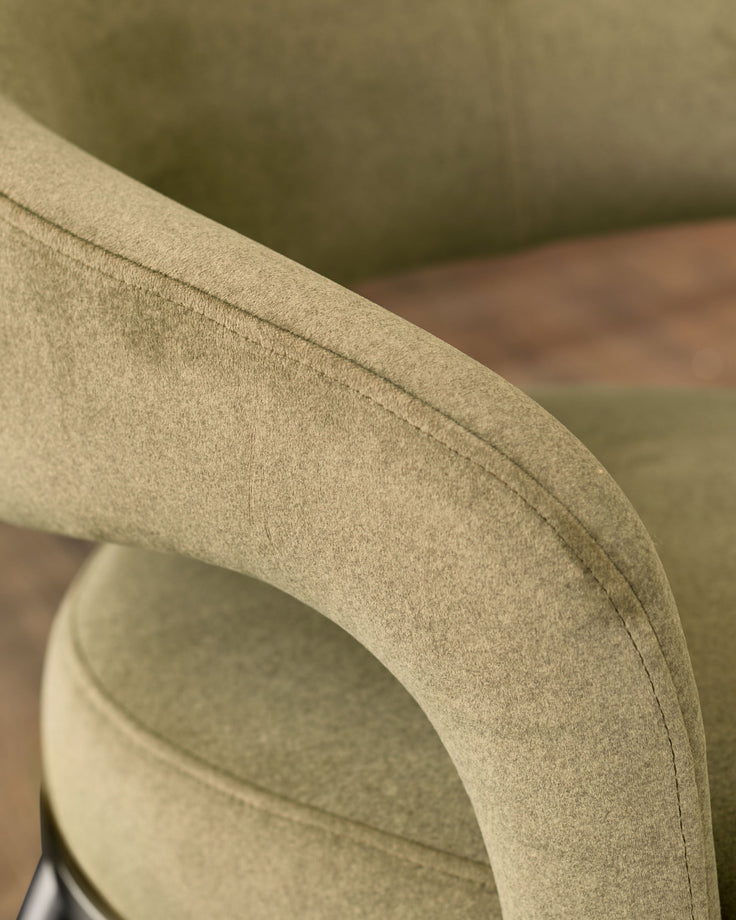Rhett dining chair in olive-green fabric, close-up detail of curved armrest and stitching.