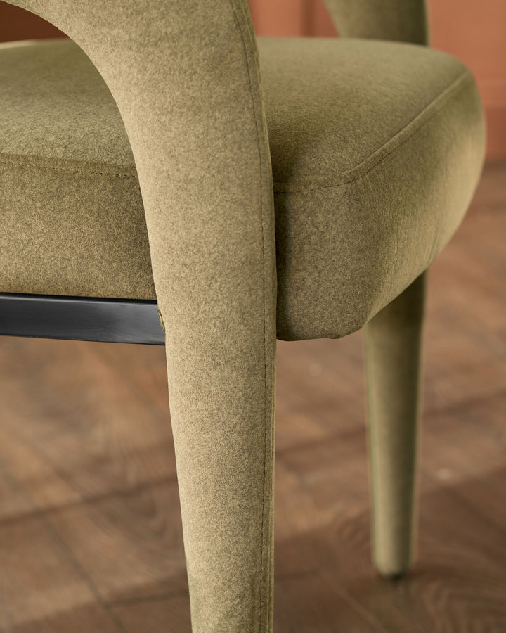 Rhett dining chair in olive-green fabric, close-up detail of curved armrest and leg with black metal frame.