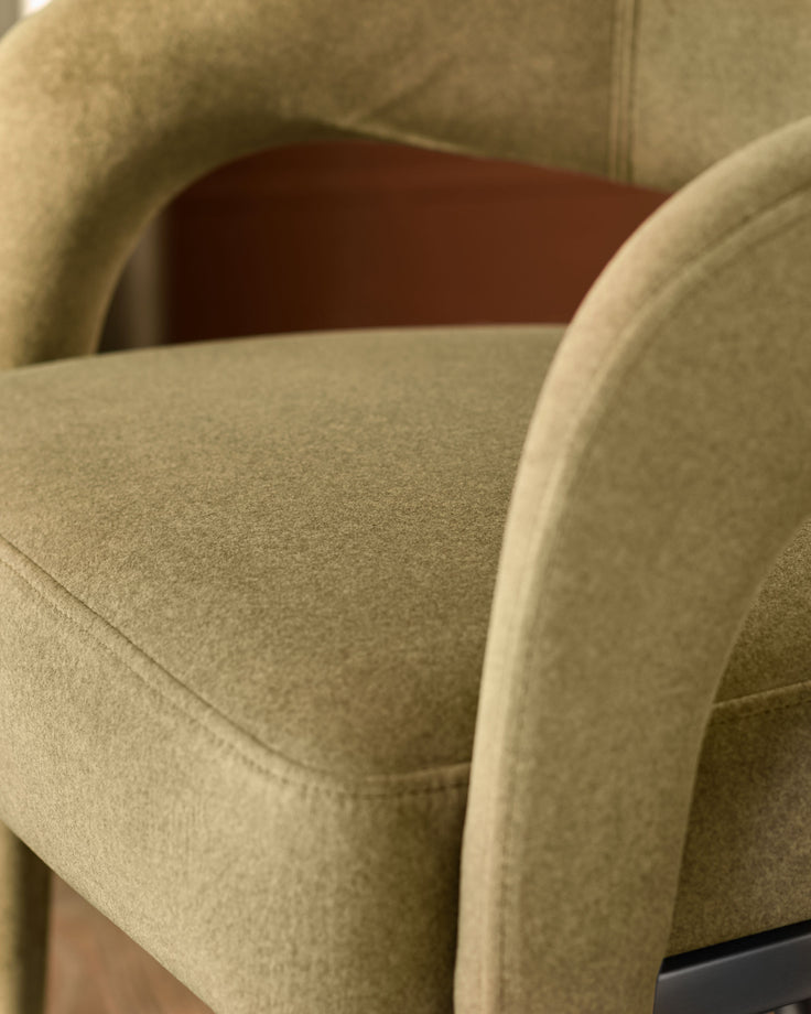 Rhett Dining Chair in olive green fabric, close-up detail of curved armrest and seat.