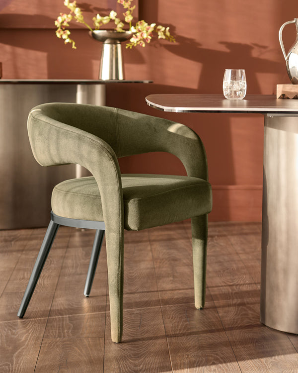 Rhett dining chair in olive green fabric with curved backrest and black metal legs, shown at dining table.