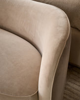 Rhiannon accent sofa in champagne velvet, close-up detail showing curved armrest and piping against herringbone rug.