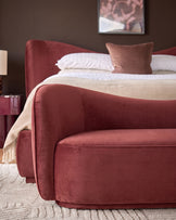 Rhiannon accent sofa in toffee red velvet, shown at an angle in a bedroom setting with white bedding and coordinating pillows.