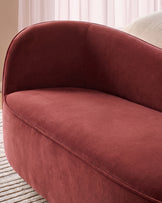 Rhiannon accent sofa in toffee red velvet, curved design with rounded backrest, shown at side angle in modern interior setting.