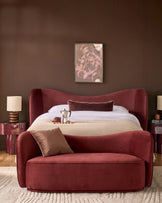 Rhiannon accent sofa in toffee red velvet, curved design, styled in bedroom setting with pillows.