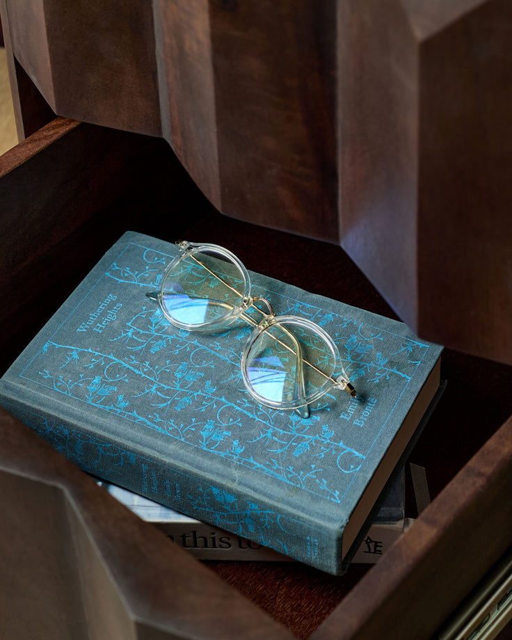 Dark mango wood bedside table with a blue book and eyeglasses resting on top.