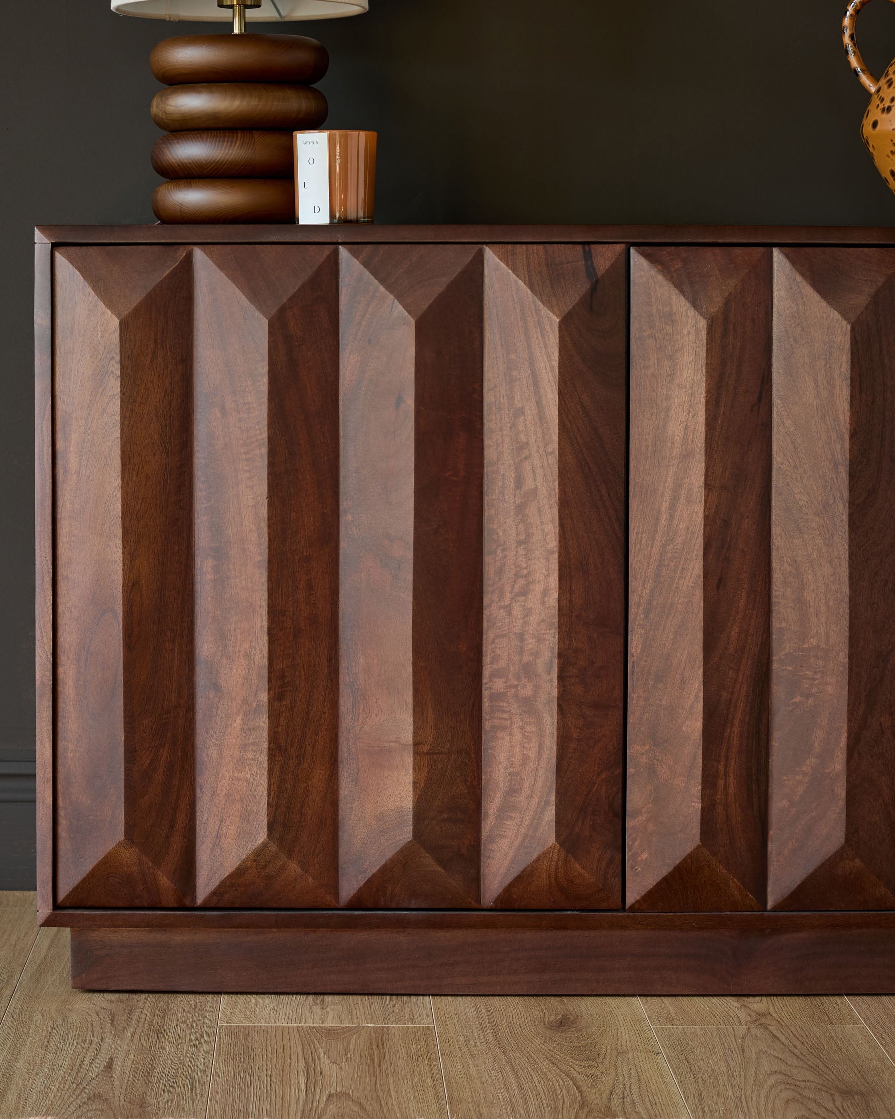 Dark mango wood sideboard with geometric chevron-pattern doors, brass lamp and decorative items on top, front view.
