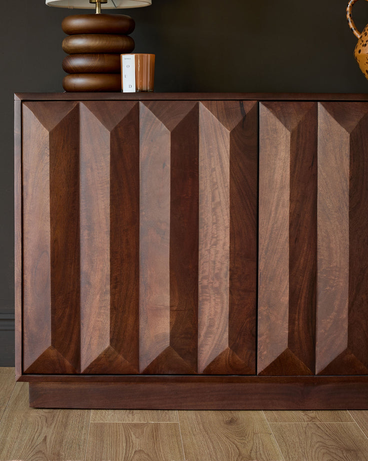 Dark mango wood sideboard with geometric chevron-pattern doors, brass lamp and decorative items on top, front view.