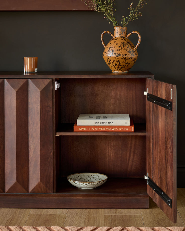 Dark mango wood sideboard with geometric panel doors, open interior shelving, and black handles displayed against grey wall.