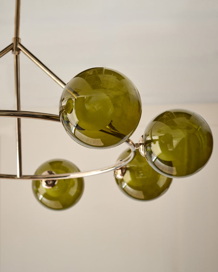 Riley 8-pendant light with olive green glass spheres and brass metal frame, photographed against white background.