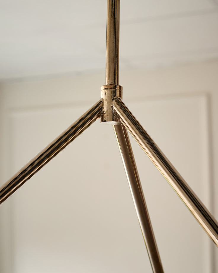 Close-up of brass tripod base structure for Riley pendant light with polished metal finish against neutral background.