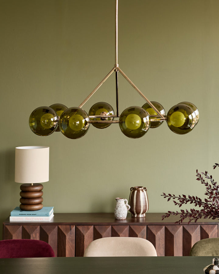 Riley 8-pendant light with olive green glass spheres and brushed brass frame, suspended above a styled console table.