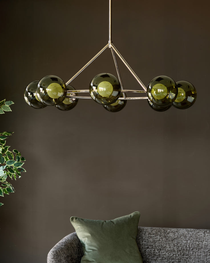 Riley 8-pendant light with olive green glass spheres and polished nickel frame, suspended above Grey sofa with green pillow.