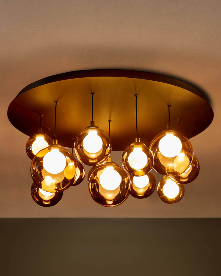 A statement chandelier with amber glass globes, hanging from a circular brass ceiling plate, creating a warm glow.