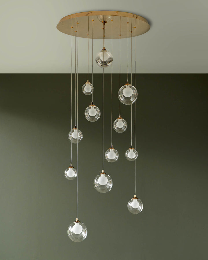 A stylish pendant light fixture with clear glass globe shades suspended at varying lengths from a round gold ceiling canopy.