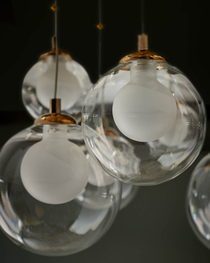 Pendant lights with clear glass orbs and copper fixings hang against a dark background. Modern lighting to brighten any space.