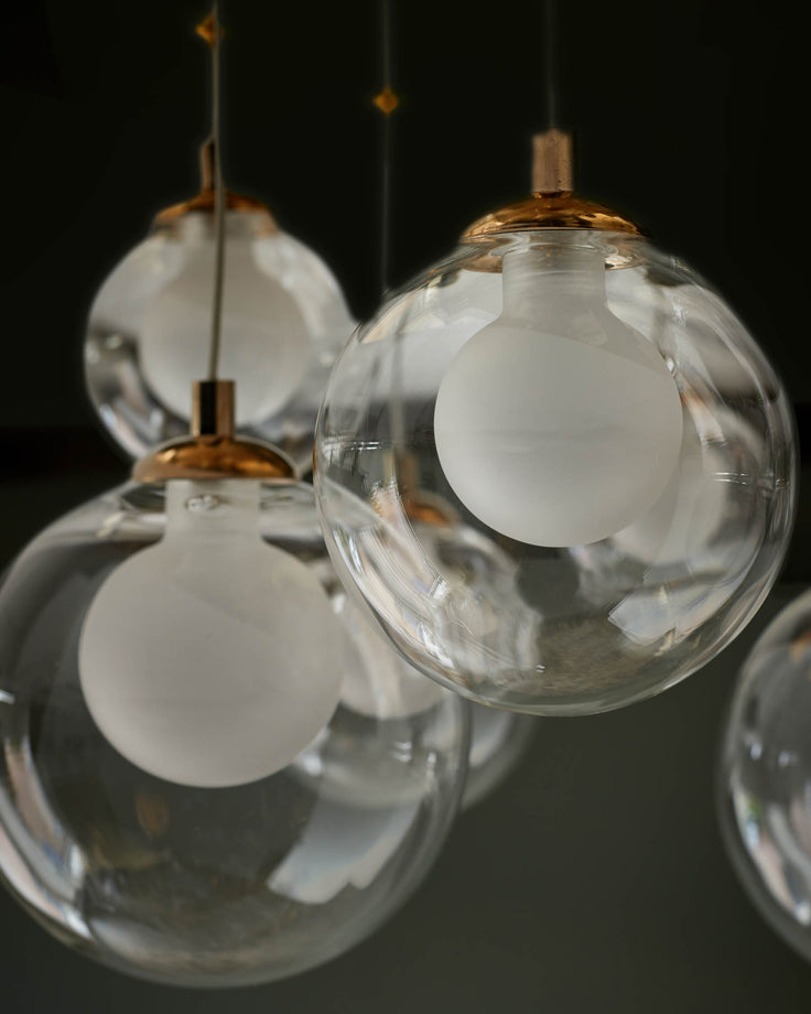 Pendant lights with clear glass orbs and copper fixings hang against a dark background. Modern lighting to brighten any space.