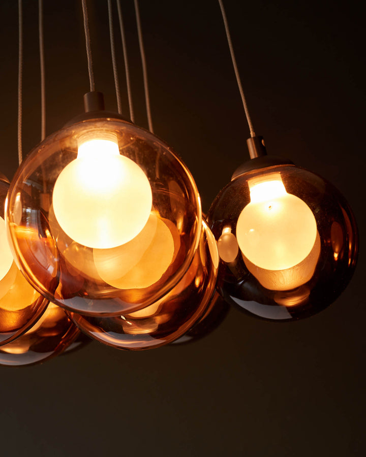 Cluster of pendant lights with smoked glass shades and bright bulbs, hanging from slender cords. Modern lighting fixture.