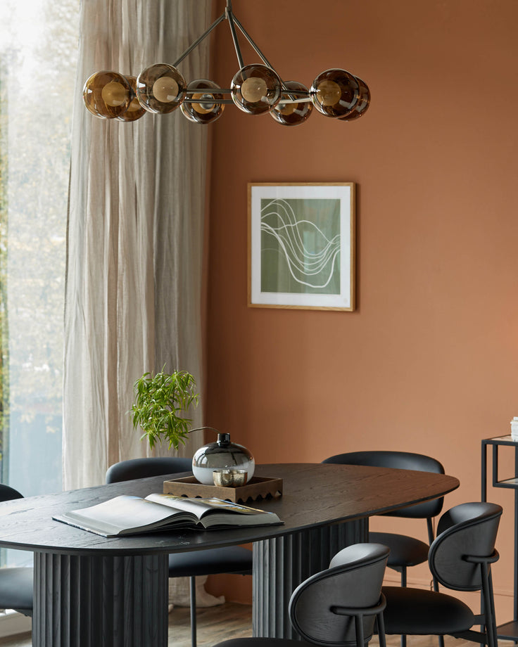 Dining set: a dark oval table with ridged base, surrounded by sleek black chairs. Modern lighting above.
