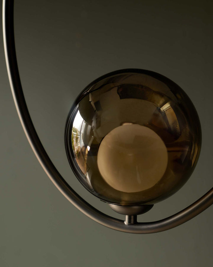 A stylish light fitting featuring a smoked glass globe and curved metal frame, perfect for adding a touch of modern elegance.