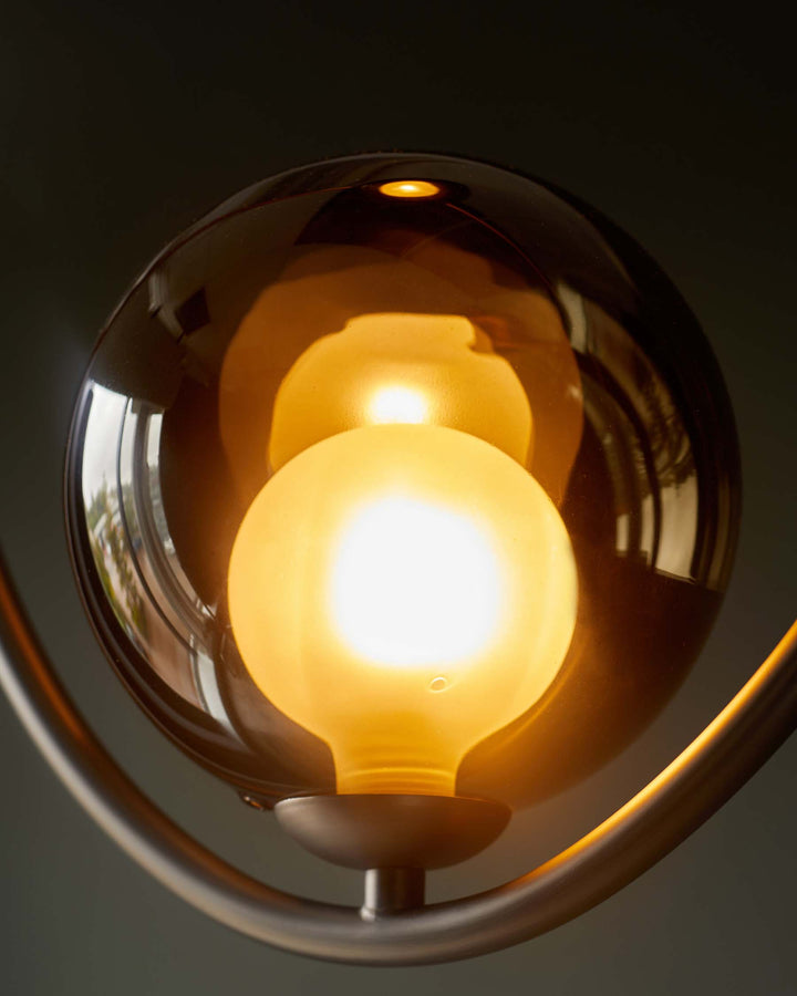 Modern light fitting with spherical tinted glass shade and illuminated bulb on a metal base.