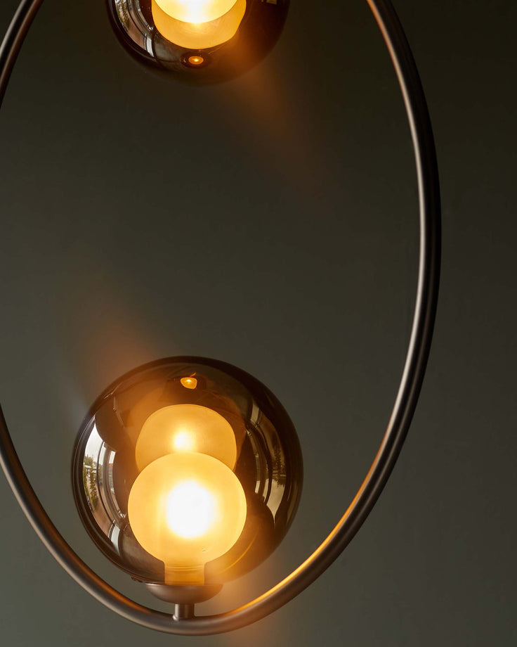 Close-up of a modern pendant light with two smoky glass globes and a circular metal frame, emitting a warm glow.